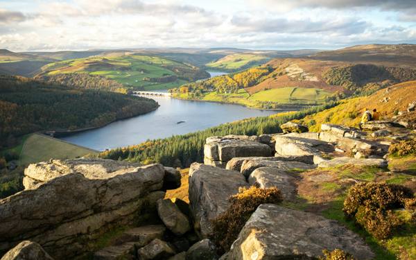 A reservoir among wooded hills seen from rocky moorland
