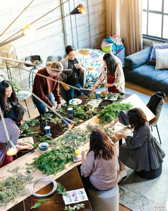 A group making flower crowns around a long studio table